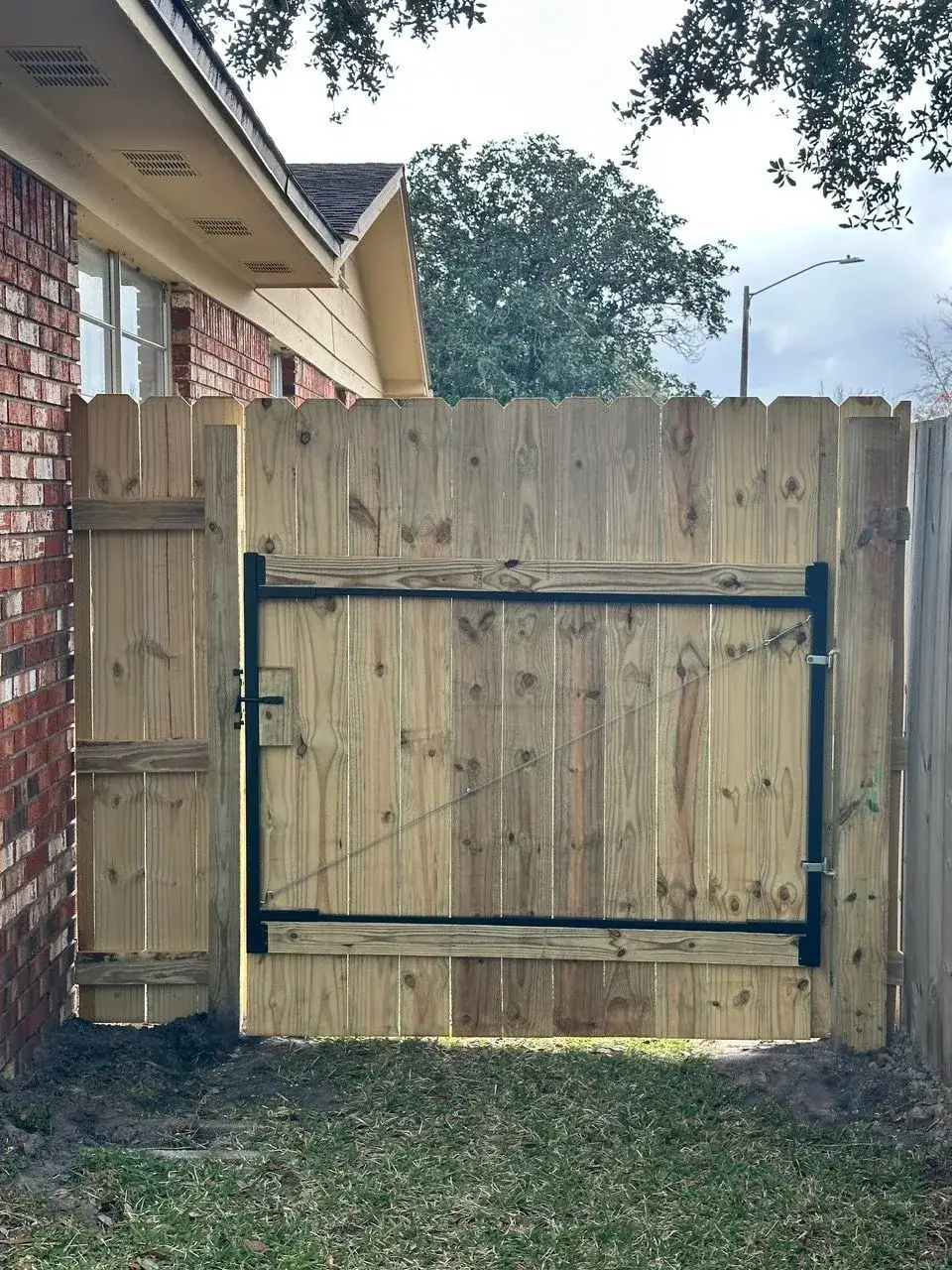 Wood gate with a steel frame installed against a brick home exterior