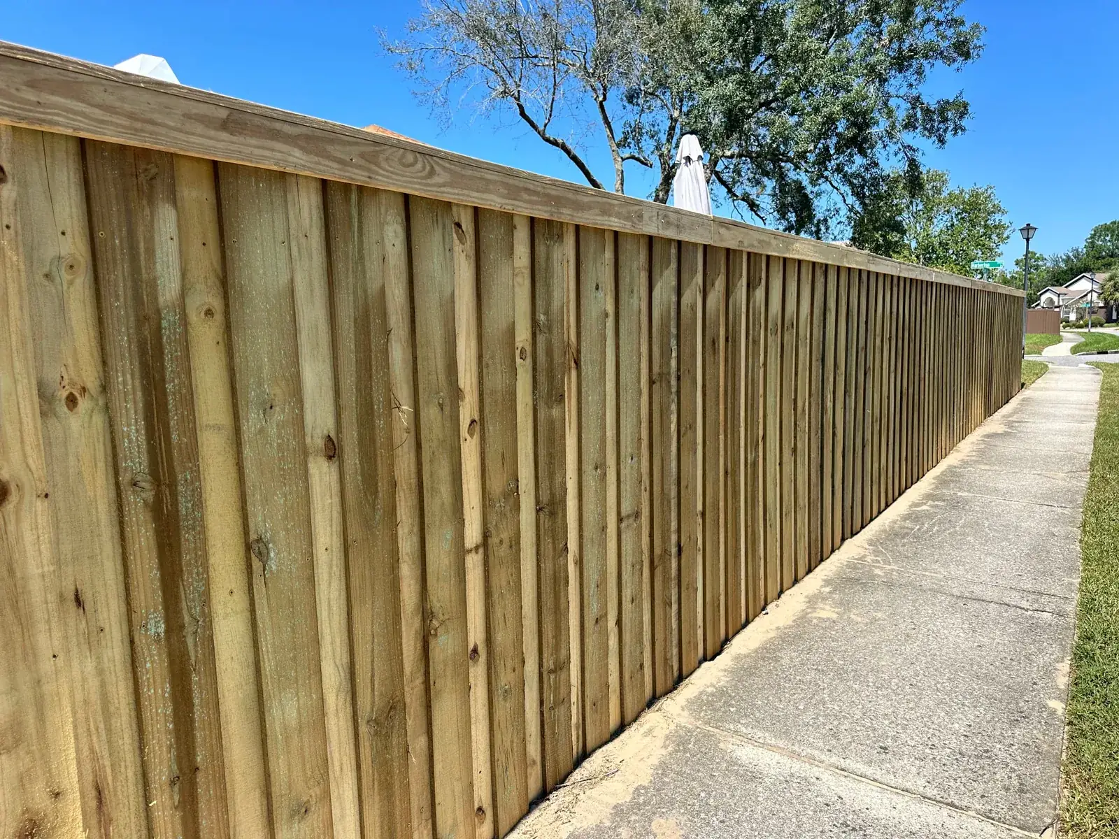 Long wood privacy fence running alongside a concrete neighborhood sidewalk