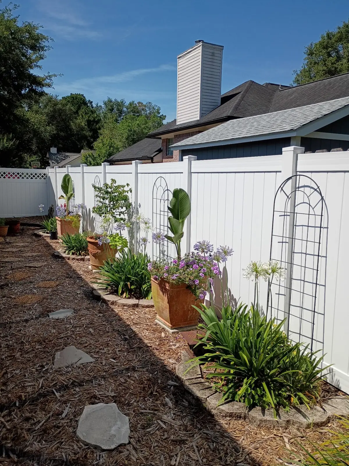 White vinyl privacy fence behind planted garden beds and a trellis