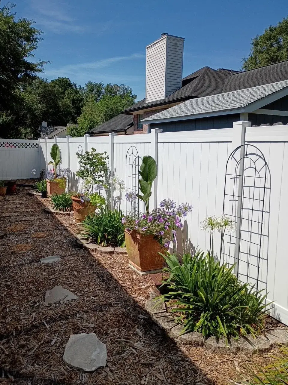 White vinyl privacy fence behind planted garden beds and a trellis