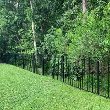 Black aluminum fence at the edge of an open yard backing to trees