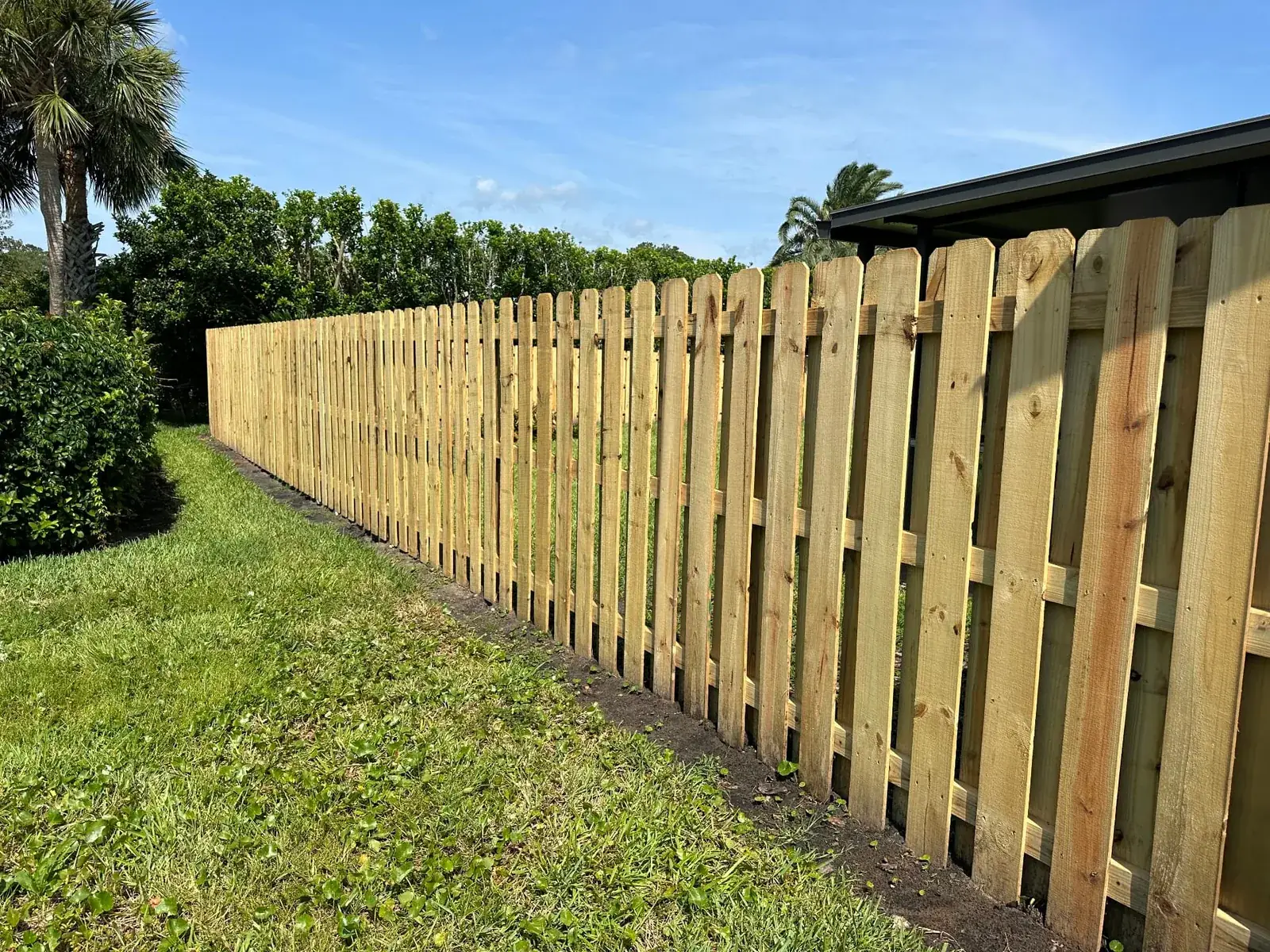 Shadowbox wood fence running alongside a hedge line at the rear of a yard
