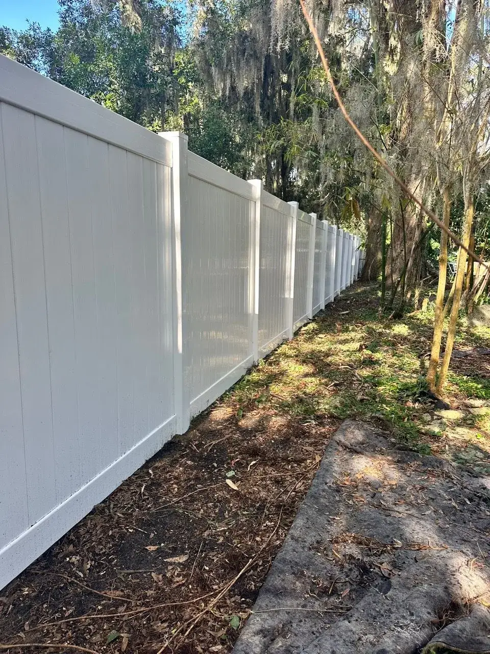 White vinyl privacy fence installed along a shaded side yard