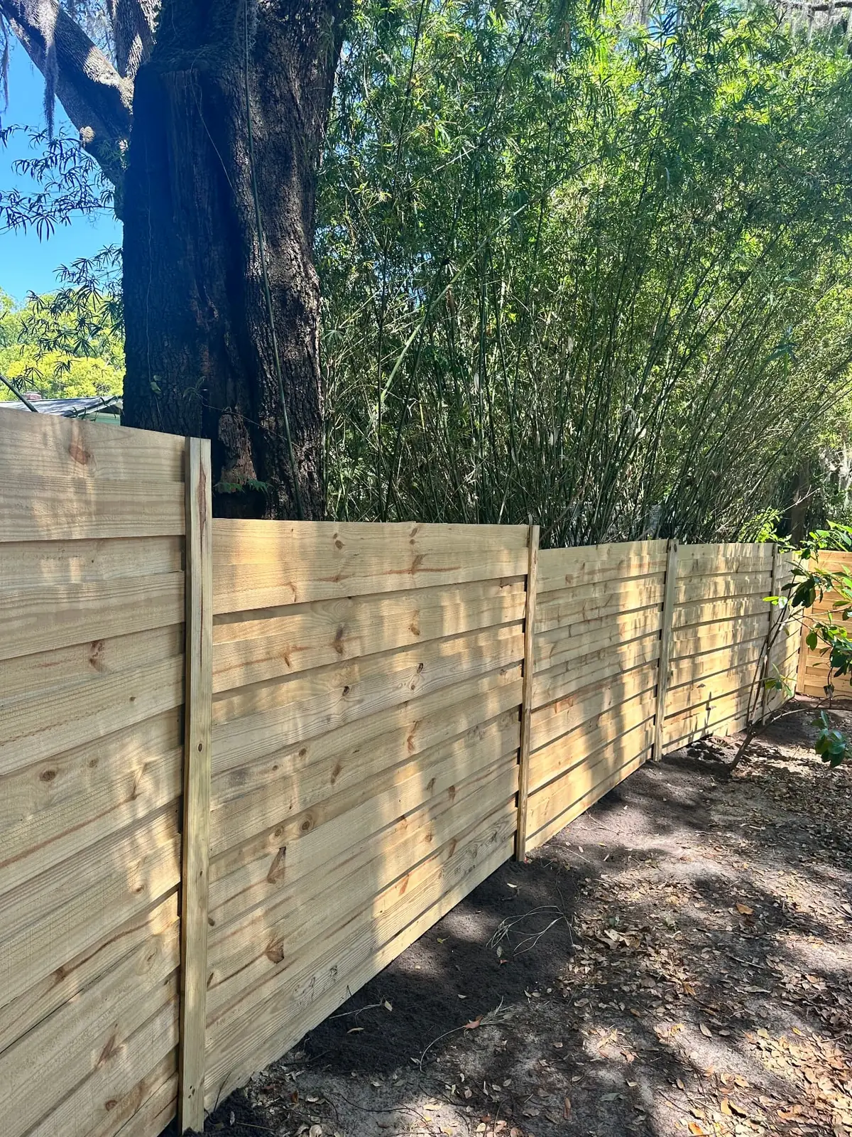 Horizontal wood privacy fence running through a wooded residential yard